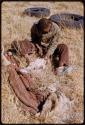 /Gishay sitting by a truck, scraping a lion skin