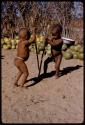 Two children digging at the ground with digging sticks