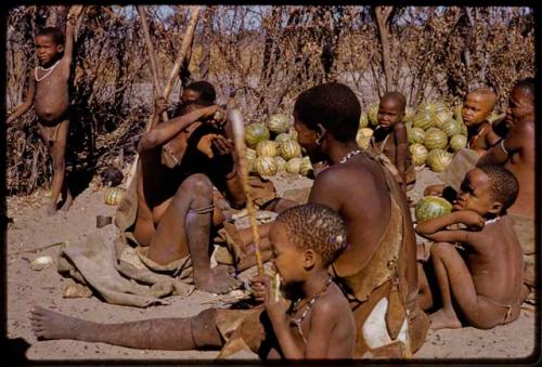 Woman scraping water root onto sieve, people sitting around her