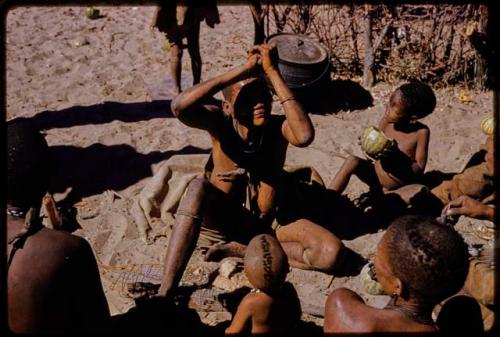 Woman squeezing juice from a water root over her face, people sitting watching her