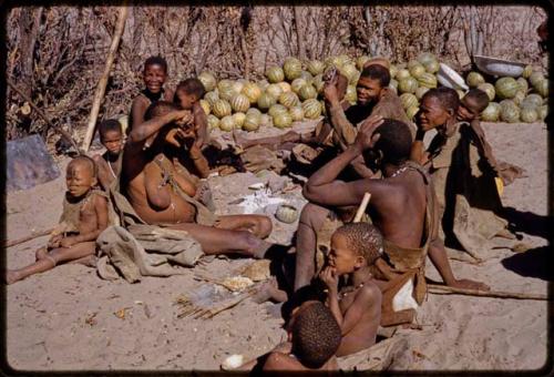 Woman squeezing juice from a water root over her face, people sitting around her