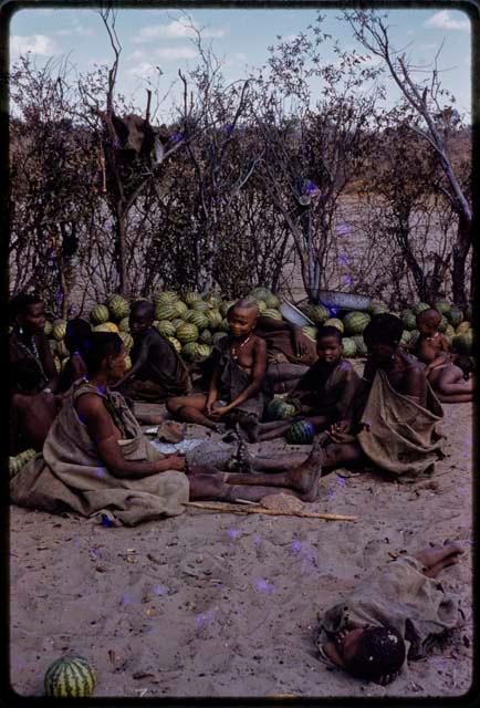 People sitting together by a pile of melons