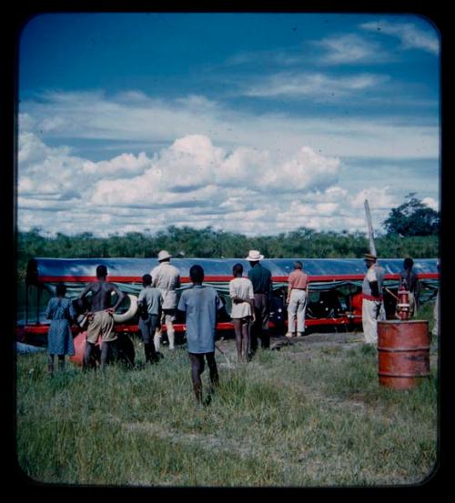 Group of people, including the expedition members, gathered near a barge at the bank of the Okavango River, seen from behind