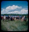 Group of people, including the expedition members, gathered near a barge at the bank of the Okavango River