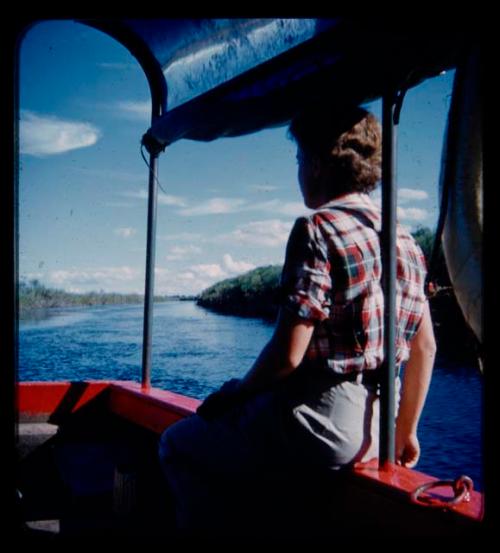 Elizabeth Marshall Thomas sitting on a rail of a barge on the Kavango River, seen from behind