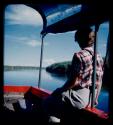 Elizabeth Marshall Thomas sitting on a rail of a barge on the Okavango River, seen from behind