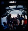 Group of people, including expedition members, riding in a barge on the Okavango River; John Marshall is fishing