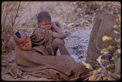 Two boys sitting, wrapped in a kaross