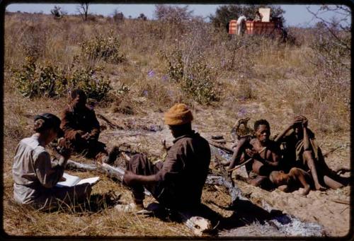 Oukwane and Gai sitting with Kernel Ledimo, /Gishay, and Lorna Marshall holding a notebook