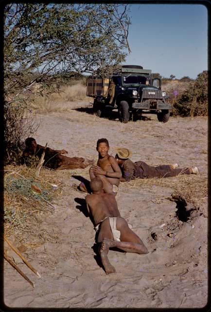 Gai, Oukwane, Kernel Ledimo, and another person lying on the ground, expedition truck in the background