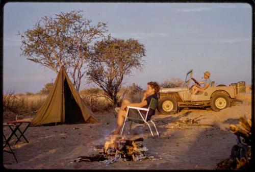 Elizabeth Marshall Thomas sitting in a camp chair, Casper Kruger sitting in expedition Jeep at camp