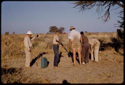 Expedition members standing around John Marshall, aiming a gun at a mamba