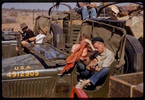 John Marshall and Elizabeth Marshall Thomas resting in expedition GMC truck, other expedition members in a truck behind