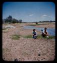 Brian Ensilin and his sister sitting by water, with cattle in the background