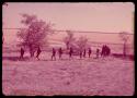 People walking in a line through the grass at the edge of a dry pan, with the men walking at the front of the line