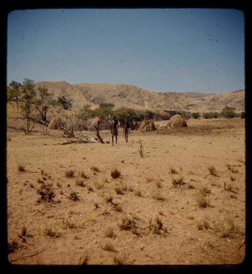 People standing, with huts in the background