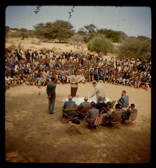 Omajetti indaba, large group of people sitting and standing around a group of men sitting next to a table