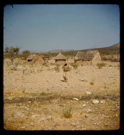 Man walking, with huts in the background