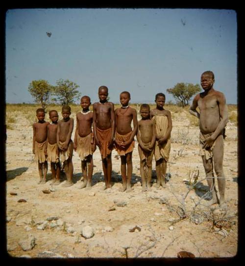 Group of children standing in a line, with a man standing next to them