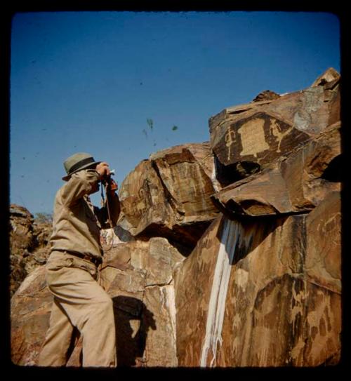 Laurence Marshall photographing petroglyphs of humans standing next to an animal skin