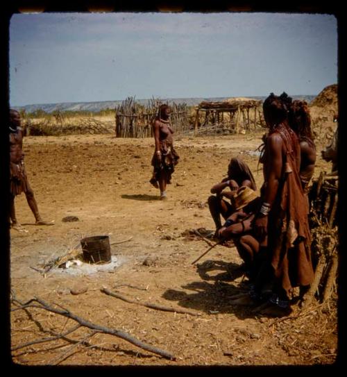 People standing and sitting near a fire with a metal container on it