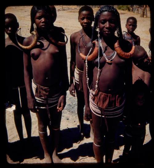 Group of women and children standing, two women wearing horns indicating eligibility for marriage, close-up