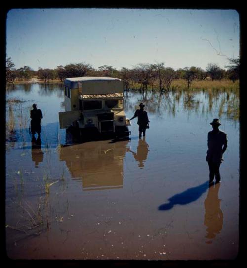 Three expedition members standing next to an expedition truck in water