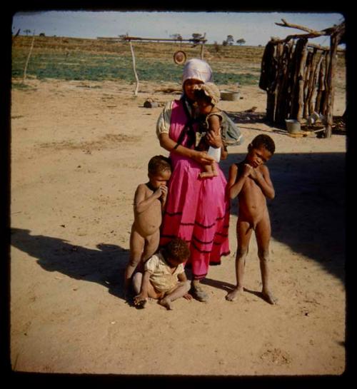 Woman wearing a dress, holding a baby, with three other children standing and sitting next to her