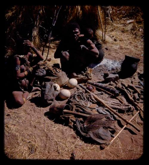 "Gao Medicine" and Di!ai sitting in front of a skerm, with Gao holding a baby, their possessions on the ground in front of them, close-up