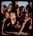 /Gao (son of /Ti!kay and N/aoka) sitting with /Gishay (younger son of "Old Gau") who is holding a model of a paauw