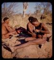 "Gao Medicine" making a plasticene model of a gemsbok, with two men sitting next to meat behind him