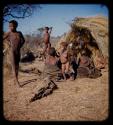 /Gishay (younger son of "Old /Gao"), "Lame ≠Gao" and N/ani standing next to a group of adults sitting in front of a skerm