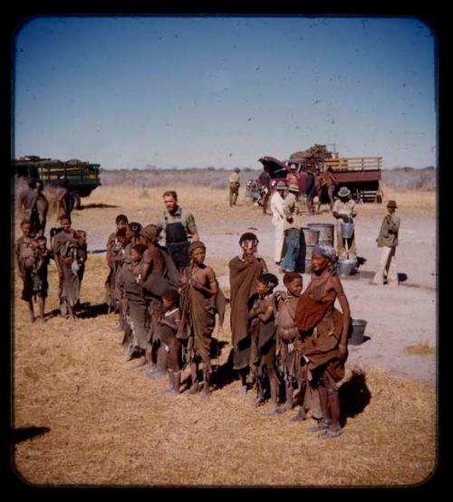 People standing in a line, with expedition trucks in the background