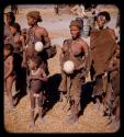 Two women holding ostrich egg shells, standing with a group of women and children