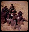 Group of women and children sitting, two wearing beads in their hair