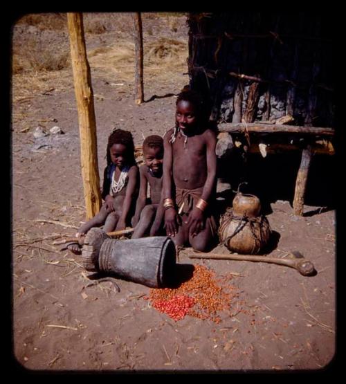 Three children sitting, with a mortar and beans on the ground in front of them