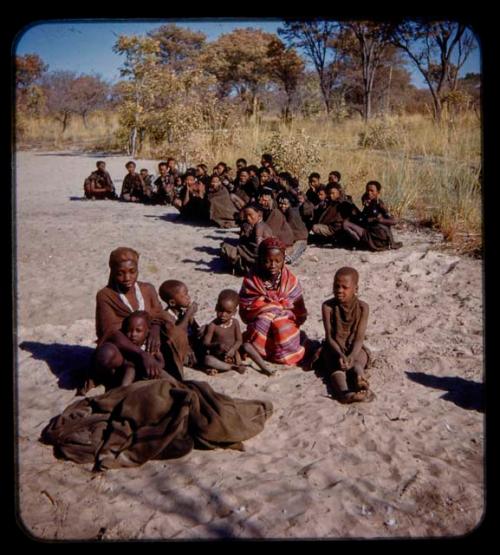 Two women sitting with children, with another group of people sitting behind them