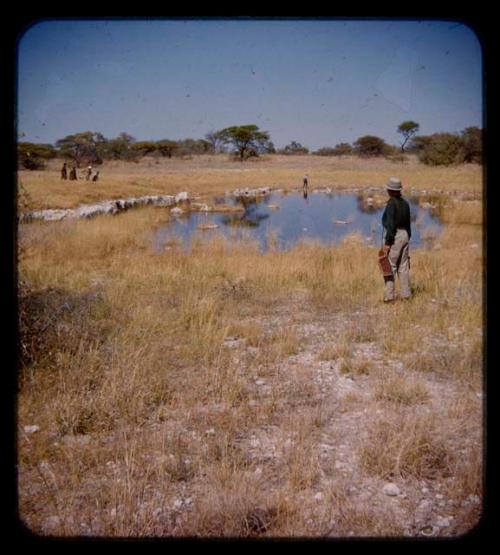 Two men standing with expedition members, looking at a snake, distant view