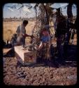 Elizabeth Marshall Thomas sitting in the expedition camp, with other expedition members standing next to her (double exposure)