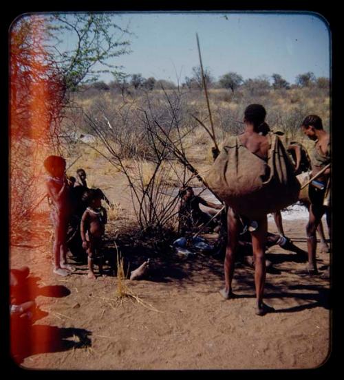 Carrying: Man carrying hunting equipment, with other people in the background