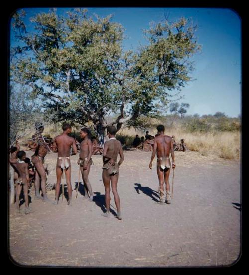 Clothes: Group of boys wearing dance rattles and standing, seen from behind