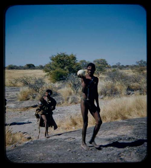 Water: Man carrying an ostrich eggshell, walking with a woman carrying a baby