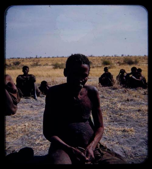 Portraits: Elderly man sitting, with other people sitting in the background