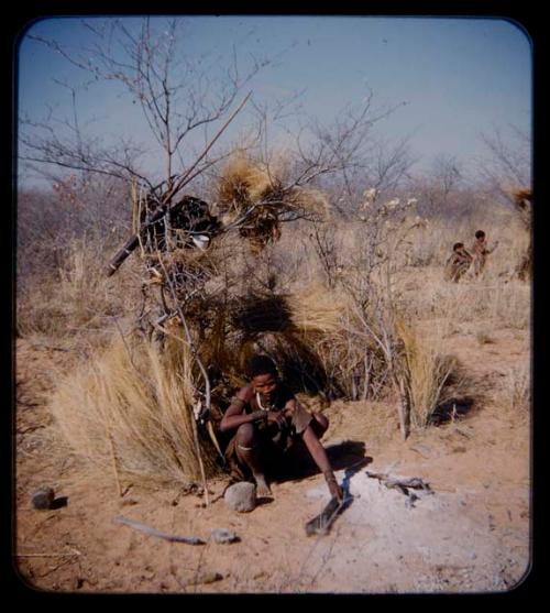 Skerm: Woman sitting at the entrance of a skerm, with fire ashes nearby