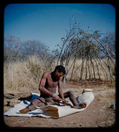 Skerm: Man sitting and working on a white animal hide