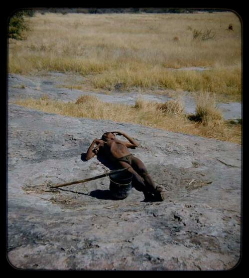 Water: Man lying down on rocks, with a pot and a carrying stick beside him