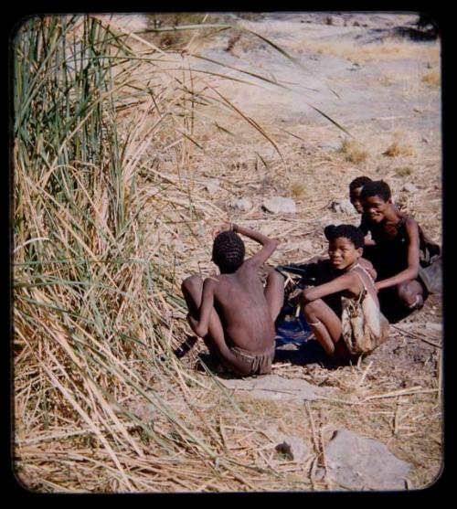 Waterhole: Man drinking water by a waterhole, with two boys and another man sitting nearby