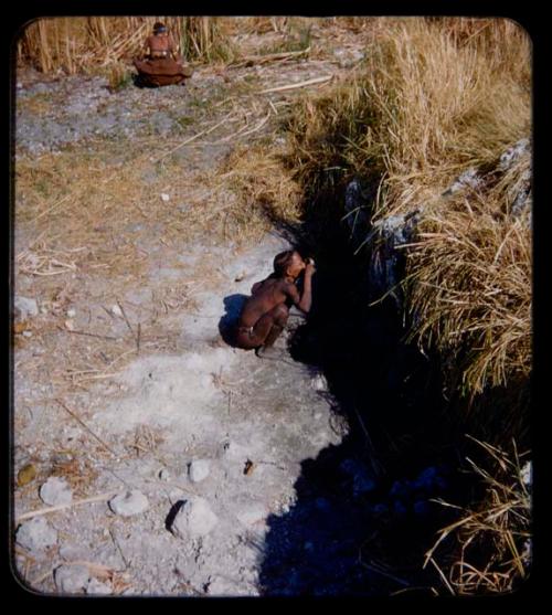 Waterhole: Man squatting and drinking water at a waterhole