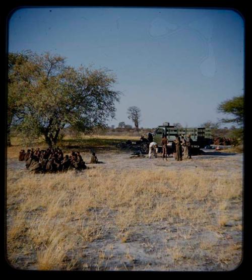 Expedition: Group of people gathered and sitting, with a green truck and other people in the background