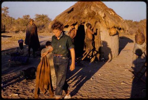 People outside a hut, Elizabeth Marshall Thomas walking and John Marshall sitting